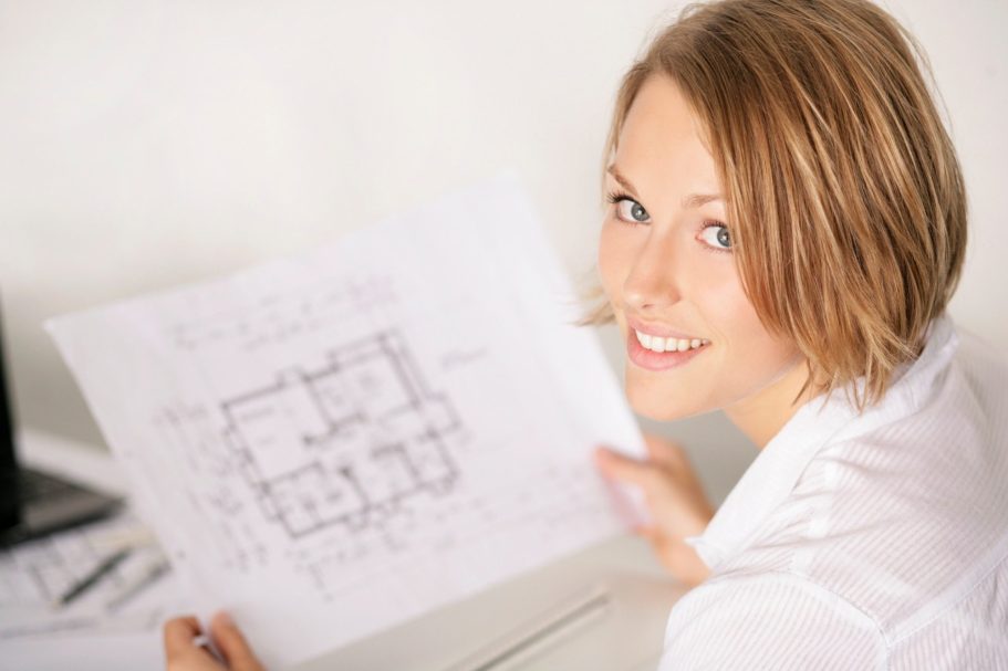 Der Hausbau Berater - Fachberater für Fertighäuser - Thomas Bärtle Junge Frau hält einen Bauplan und lächelt in die Kamera.